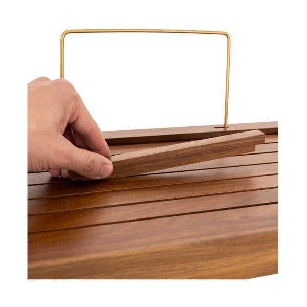 A close-up of a hand lifting a wooden piece from a slatted wooden surface with a gold metal handle, shown against a plain white background.