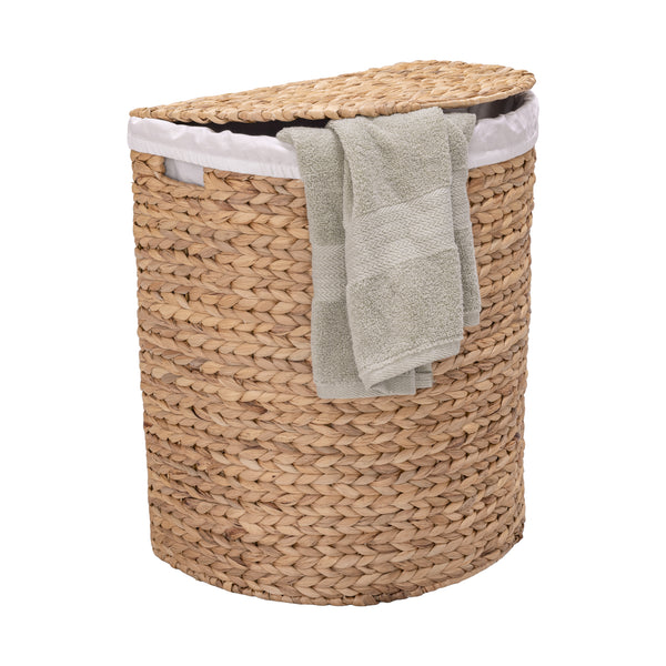 A natural woven water hyacinth laundry hamper with a matching lid, lined with white fabric and draped with a light gray towel, shown on a solid white background.