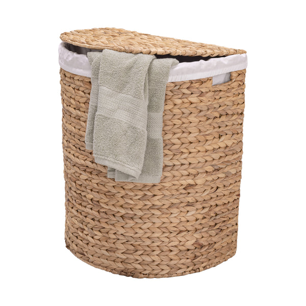 A natural woven water hyacinth laundry hamper with a matching lid, lined with a white fabric, and shown with two folded light gray towels draped over the side, on a solid white background.