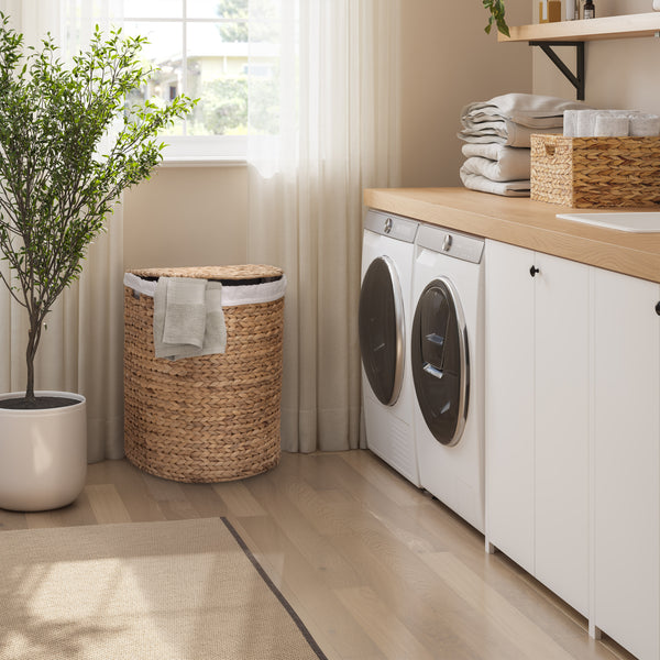 A bright, modern laundry room with a natural woven wicker laundry hamper with a folded towel, positioned next to a window and a white washing machine and dryer.