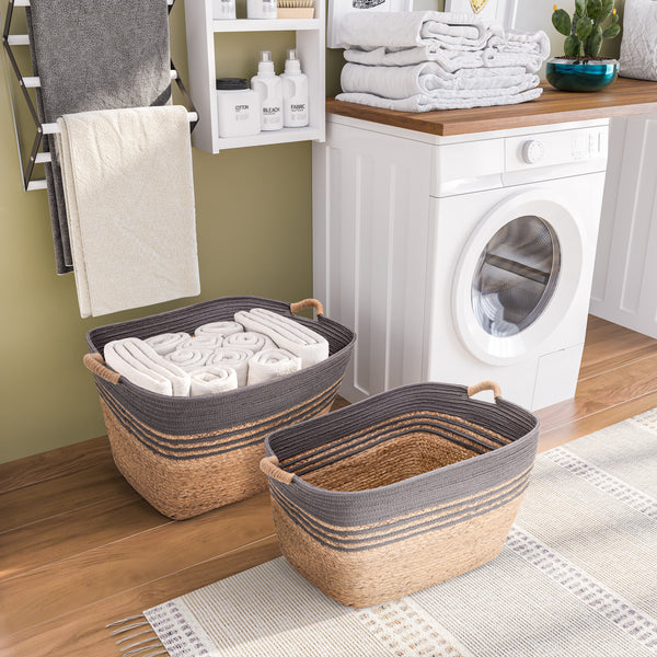 Two woven storage baskets with dark gray ribbed fabric rims and natural tan woven bases are shown in a bright laundry room. One basket is filled with folded white towels, and the other is empty.